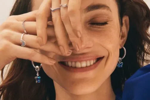 Woman covering half of her face with pandora jewellery on her hand.
