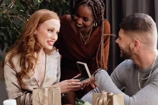 2 friends watching another friend open a gift from Warren James